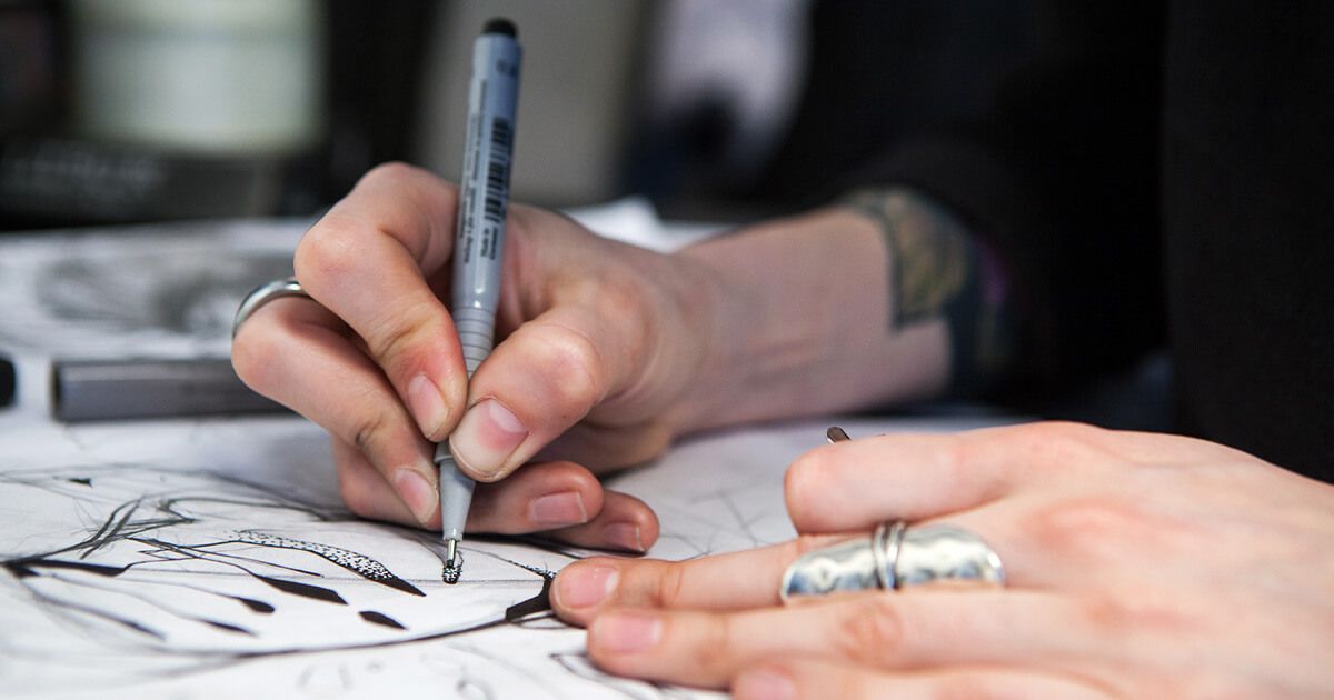 Tattoo artist using a fine-tip pen to sketch tattoo art.