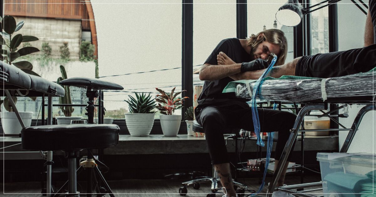 Male tattoo artist working on client's leg.