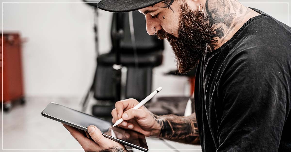 Male tattoo artist drawing on tablet.